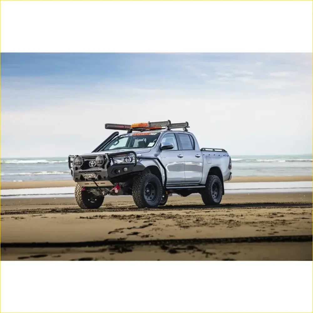 Silver toyota hilux pickup with black off-road rockarmor rock pack bullbar and rock sliders shown from the back side